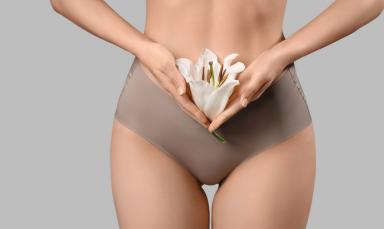 Woman in underwear with white lily flower on grey background, closeup